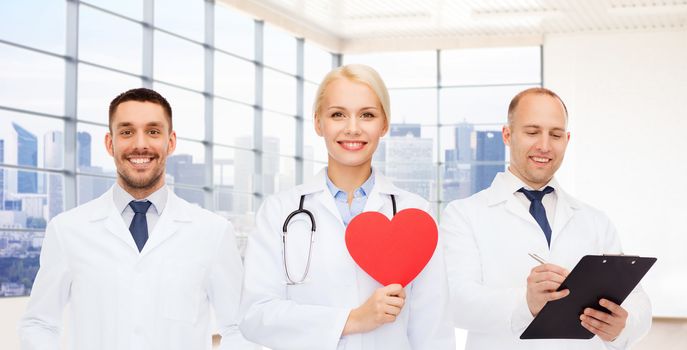 medicine, cardiology, healthcare and people concept - happy young doctors cardiologists with red heart over clinic background