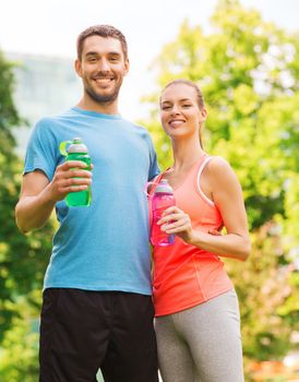 fitness, sport, friendship and lifestyle concept - smiling couple with bottles of water outdoors