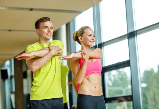 sport, fitness, lifestyle and people concept - smiling man and woman stretching in gym