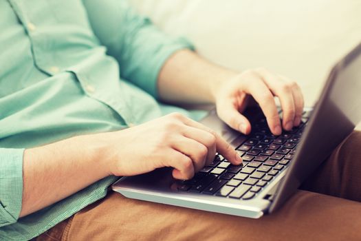 technology, home and lifestyle concept - close up of man working with laptop computer and sitting on sofa at home