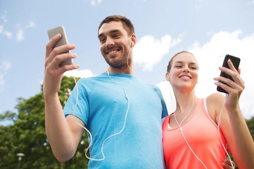 fitness, sport, training, technology and lifestyle concept - two smiling people with smartphones and earphones outdoors