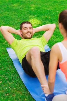 fitness, sport, training, teamwork and lifestyle concept - smiling man with personal trainer doing exercises on mat outdoors