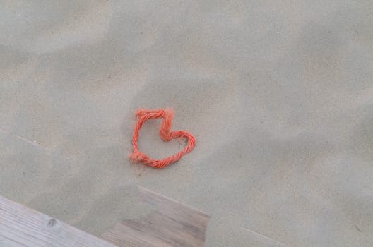 A red rope in heart shape lying in the sand. Beach background. Top View