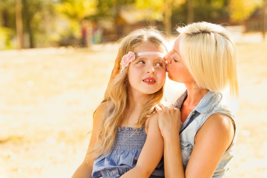 Beautiful, happy mother kissing her daughter in the nature