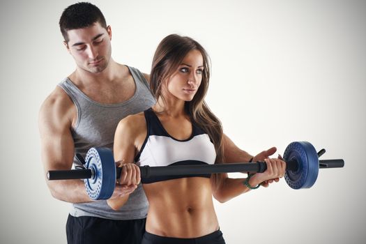 Young beautiful woman practicing Biceps muscle group with personal trainer.