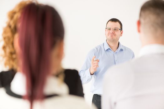 Friendly business man explaining plan of work in front of coworkers. The team is listening.