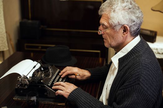 Retro Senior man writer with glasses writing on Obsolete Typewriter.