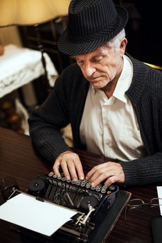 Retro Senior man writer with hat, writing on Obsolete Typewriter.