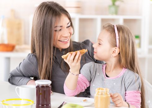 Mother and daughter breakfast in the kitchen. Cute little girl eats bread with peanut butter.