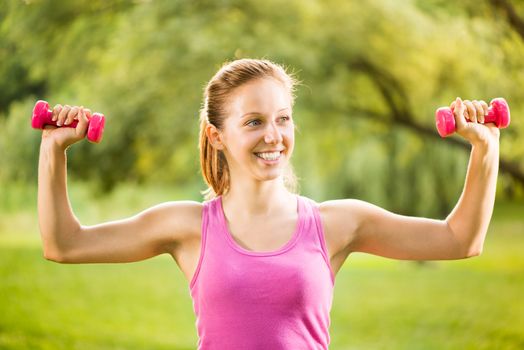 Portrait of Beautiful young woman exercising with weights in the park.