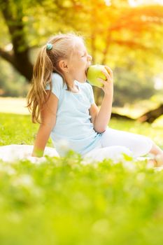 Cute little girl in the park eating an apple.