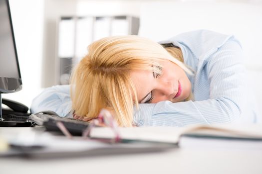 Young businesswoman sleeping on her desk next to documents late in the office. 