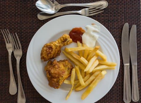 Pictured fried chicken with chips served on white dish at the restaurant, view from above.