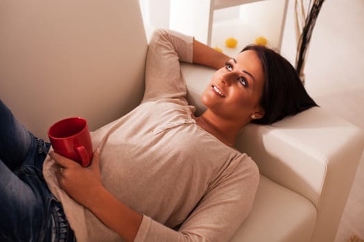 Beautiful young woman resting on sofa with morning coffee 