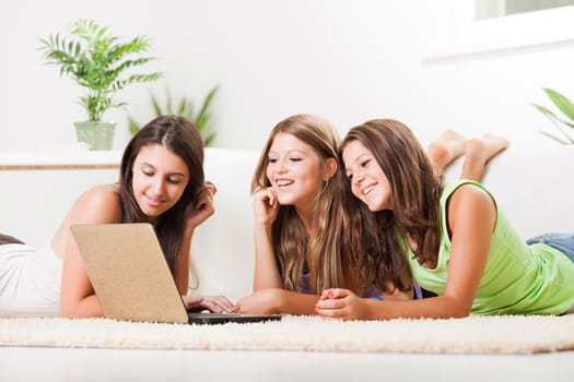 Beautiful teenage girls lying on the carpet with laptop and surfing in the internet