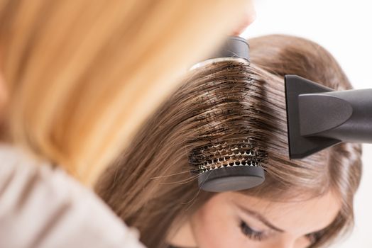 Drying long brown hair with hair dryer and round brush.