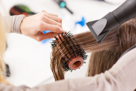 Drying long brown hair with hair dryer and round brush. Close-up.