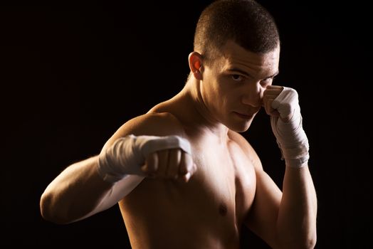 Young Fighter on black background in attack position. Only Boxing Straps on his hands.