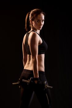 Beautiful woman with dumbbells standing on black background.