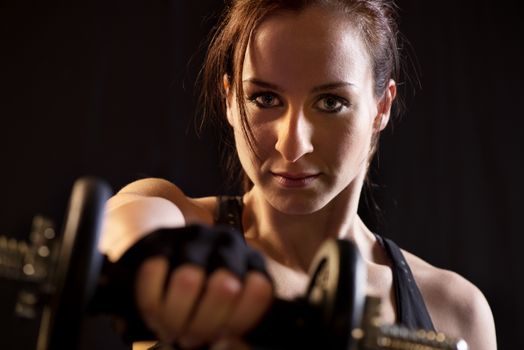 Portrait of a beautiful woman exercising with dumbbells on black background.