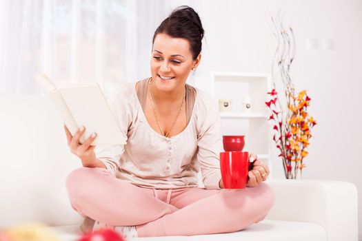 Beautiful young woman resting with book at home