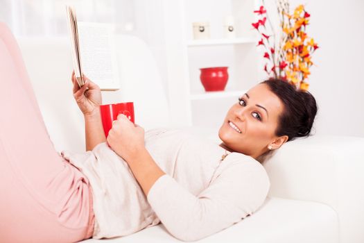 Beautiful young woman resting with book at home