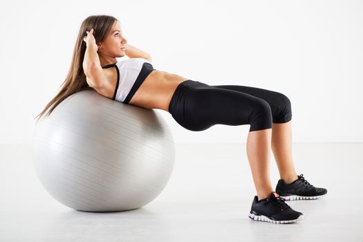 Young Beautiful Girl exercising and lifting the weights with Exercise Ball in Gym.