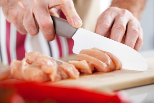 Senior Male Hands Cutting Chicken filet on the kitchen board.