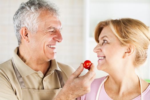 Senior Couple having fun in the kitchen and eating Red cherry tomato.