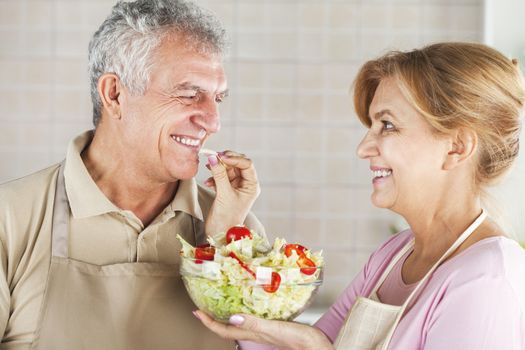 Happy Senior Couple eating salad in the kitchen, and have a fun.