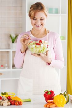 Beautiful Senior woman in the kitchen eating salad.