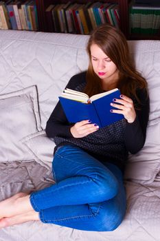Portrait of beautiful young woman sitting on a sofa at home, reading a book . Girl reading a book.