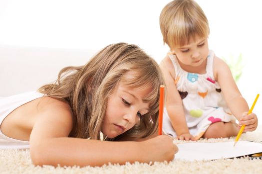 Two beautiful little girls drawing with color crayons on the floor
