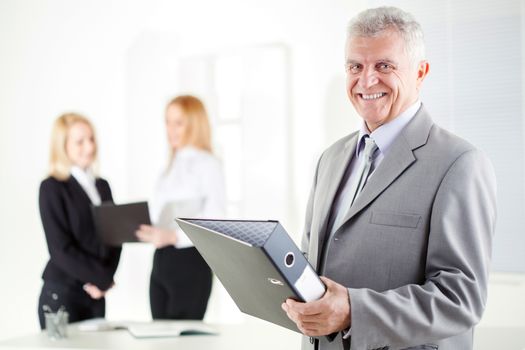 Happy senior businessman with documents standing in the office. Looking at camera. Selective Focus.