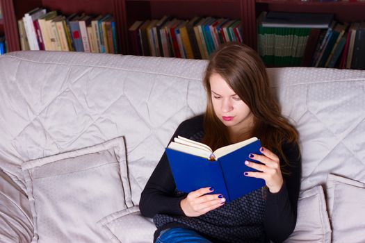 Portrait of beautiful young woman sitting on a sofa at home, reading a book . Girl reading a book.