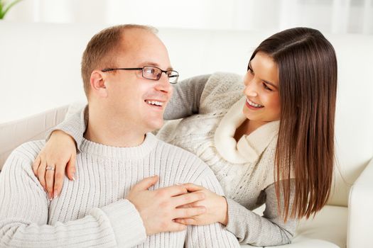 Happy beautiful Young couple sitting and hugging in home interior. Looking at camera.