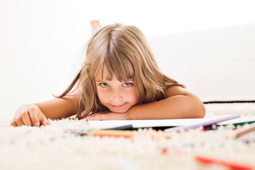 Cute little girl with color crayons lying on the carpet