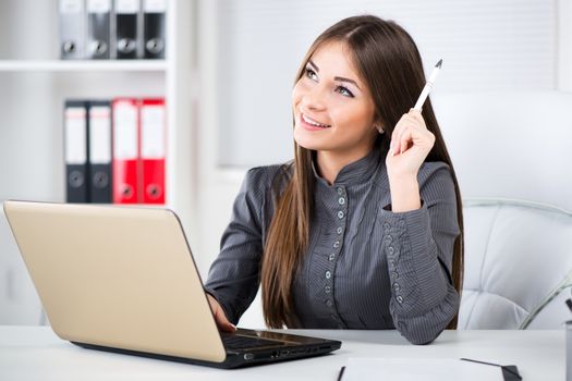 Businesswoman in the office, sitting, thinking and holding pencil in one hand.