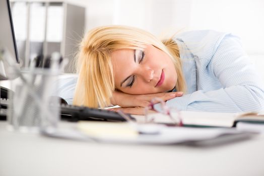Young businesswoman sleeping on her desk next to documents late in the office.