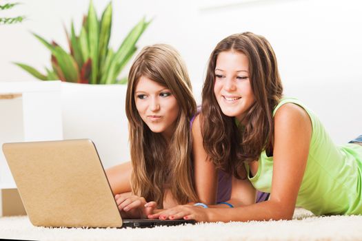 Two Beautiful teenage girls lying on the carpet and surfing internet on laptop