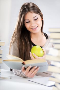 Beautiful Student girl sitting with apple between many books and learning.