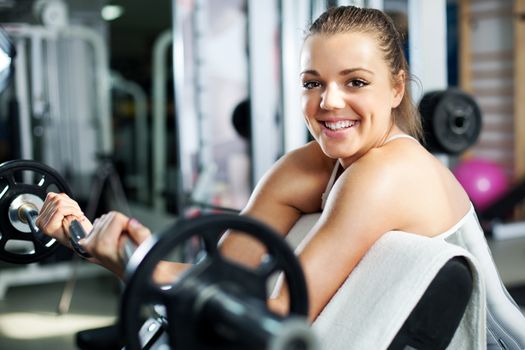 Cute Sporty young woman doing exercise in a fitness center. She is working exercises to strengthen her bicep.