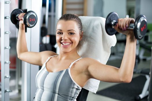 Cute Sporty young woman doing exercise in a fitness center. She is working exercises to strengthen her shoulder.