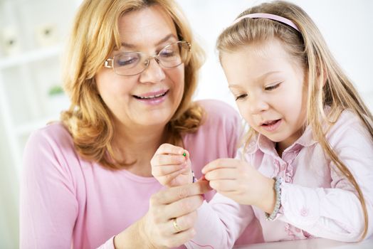 Young cute girl making bead bracelets with Grandmother