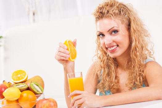 Beautiful young woman squeezes orange juice in the glass