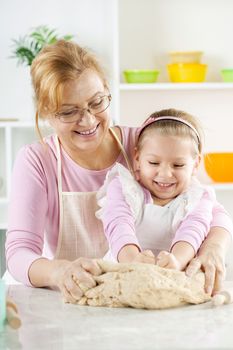 Beautiful, happy grandmother and granddaughter knead the dough together in the Kitchen. 