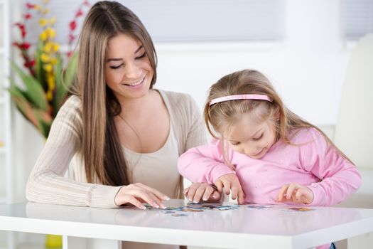 Mother and daughter playing at home. They stacking Jigsaw Puzzle.