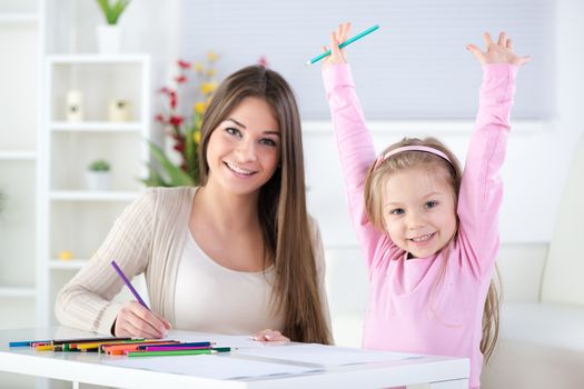 Mother and daughter at home. They drawing with colored pencils.