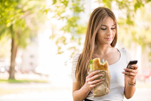 Portrait of beautiful young woman taking a break for breakfast and using a Cell Phone Outdoors.