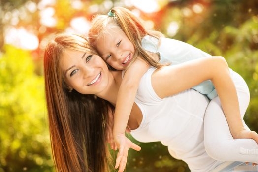 Beautiful mother and daughter having fun in the park on spring day. Young mother piggybacking his daughter.